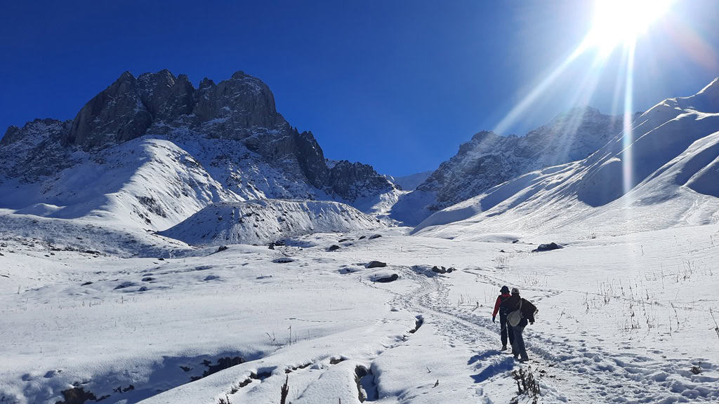 Kazbegi Travel Guide 2026: Best things to do, Hiking Trails & Essential Tips to visit Kazbegi, Georgia 18 Snow-covered mountain landscape with hikers trekking in the snow, bright sun, and clear blue sky, perfect for adventure travel and outdoor exploration.